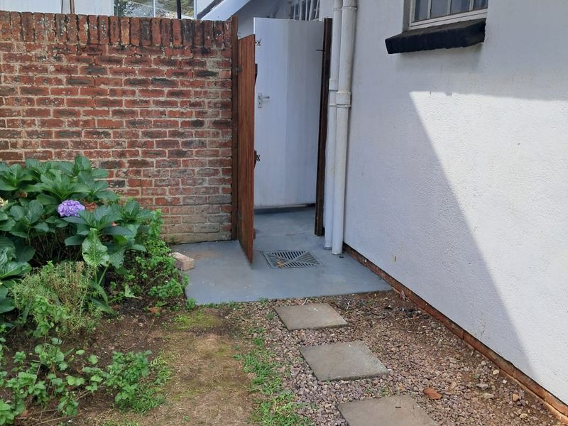 A rear exterior view of the cottage featuring a brick boundary wall, a stone pathway, and access to a side entrance.