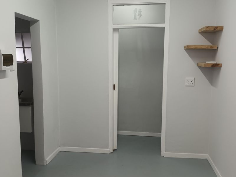 A clean, neutral hallway featuring floating wooden shelves, an air conditioning unit, and a doorway leading to an adjacent room.