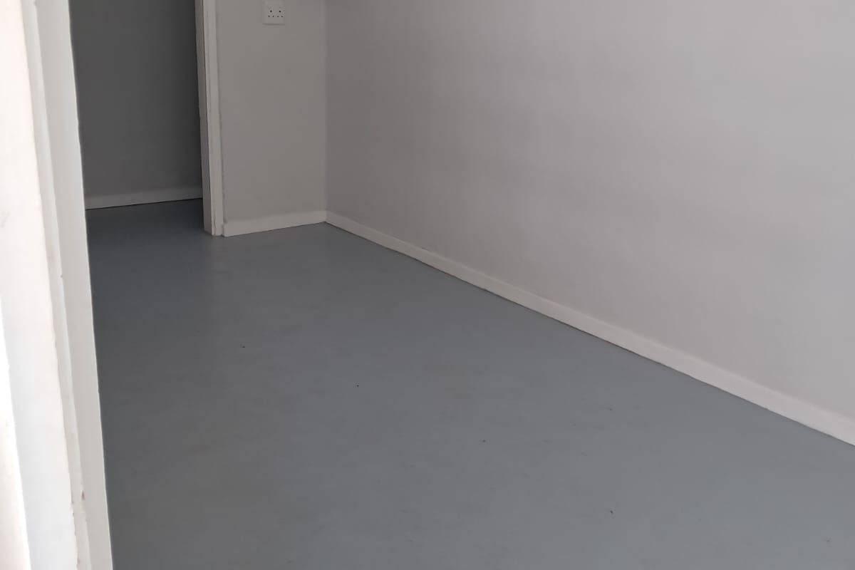 A clean, empty bedroom featuring neutral grey painted floors, white walls, and minimalist built-in floating corner shelves.