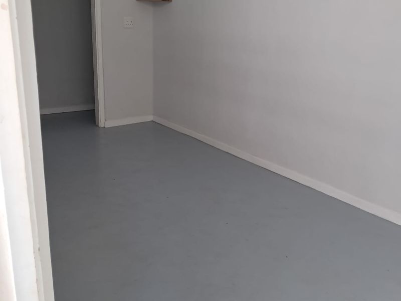 A clean, empty bedroom featuring neutral grey painted floors, white walls, and minimalist built-in floating corner shelves.