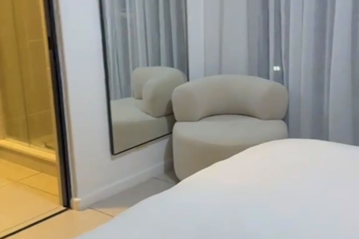 A modern bedroom featuring neutral tones, tiled flooring, and an adjoining en-suite bathroom with a glass-enclosed shower.