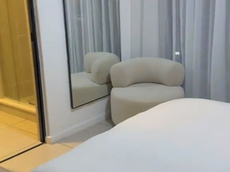 A modern bedroom featuring neutral tones, tiled flooring, and an adjoining en-suite bathroom with a glass-enclosed shower.