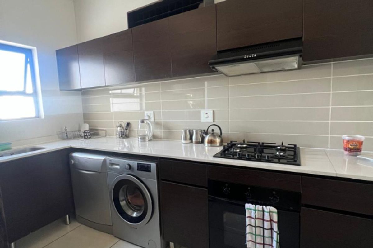 Modern kitchen featuring dark wood cabinetry, stone countertops, gas hob, built-in oven, extractor fan, and tiled backsplash.
