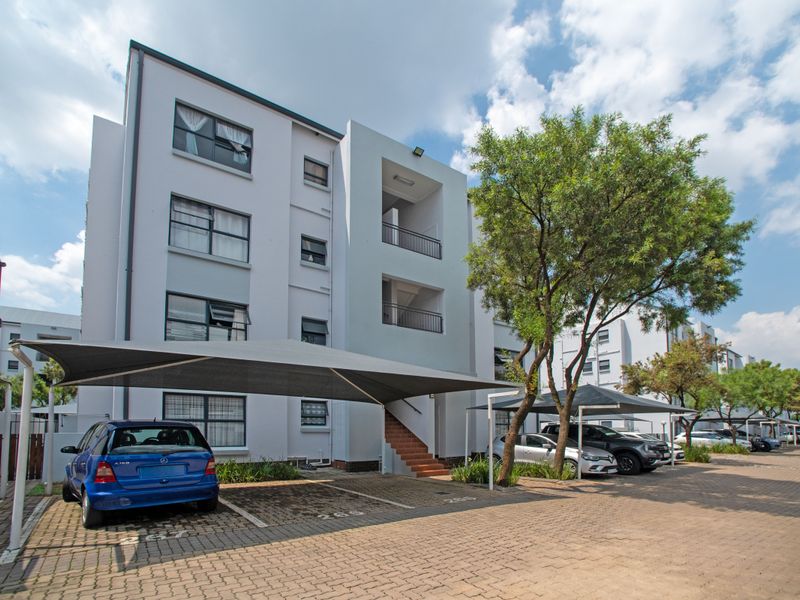 Exterior view of a multi-story apartment complex featuring paved parking areas with shade cloth carports and accessible staircases.