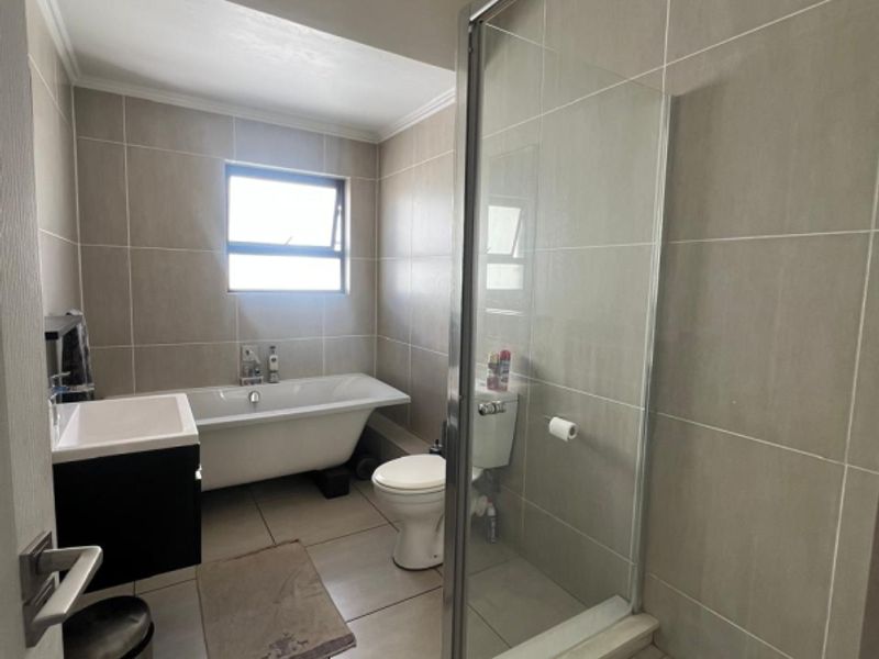 Modern bathroom featuring a freestanding bathtub, separate glass-enclosed shower, vanity cabinet, and neutral floor-to-ceiling tiling.