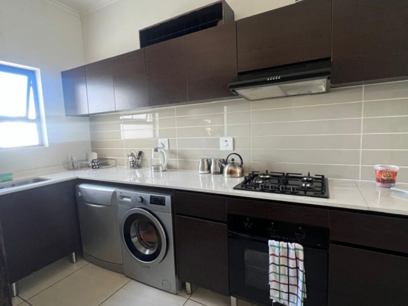 Modern kitchen featuring dark wood cabinetry, stone countertops, gas hob, built-in oven, extractor fan, and tiled backsplash.
