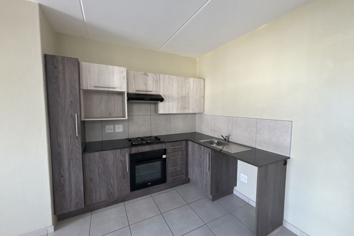 A modern, compact kitchen featuring two-tone cabinetry, dark countertops, built-in oven and hob, and neutral tiled flooring.