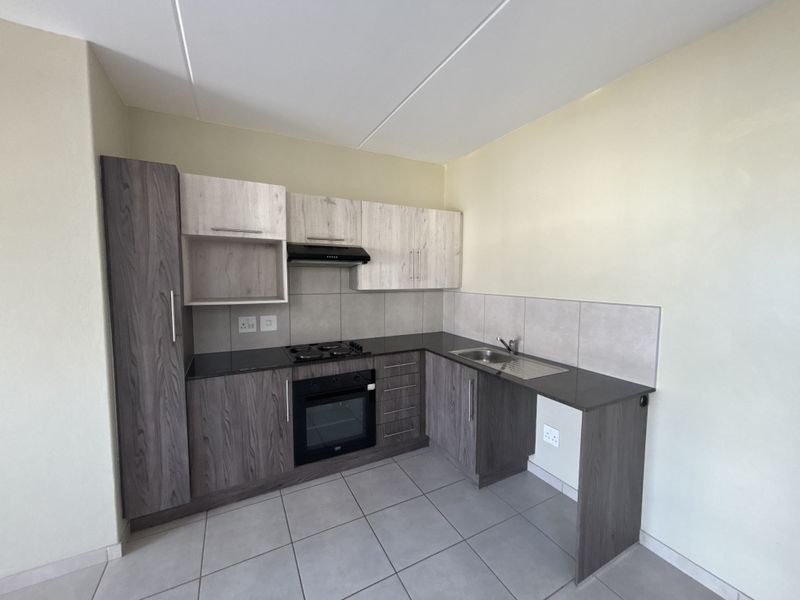 A modern, compact kitchen featuring two-tone cabinetry, dark countertops, built-in oven and hob, and neutral tiled flooring.