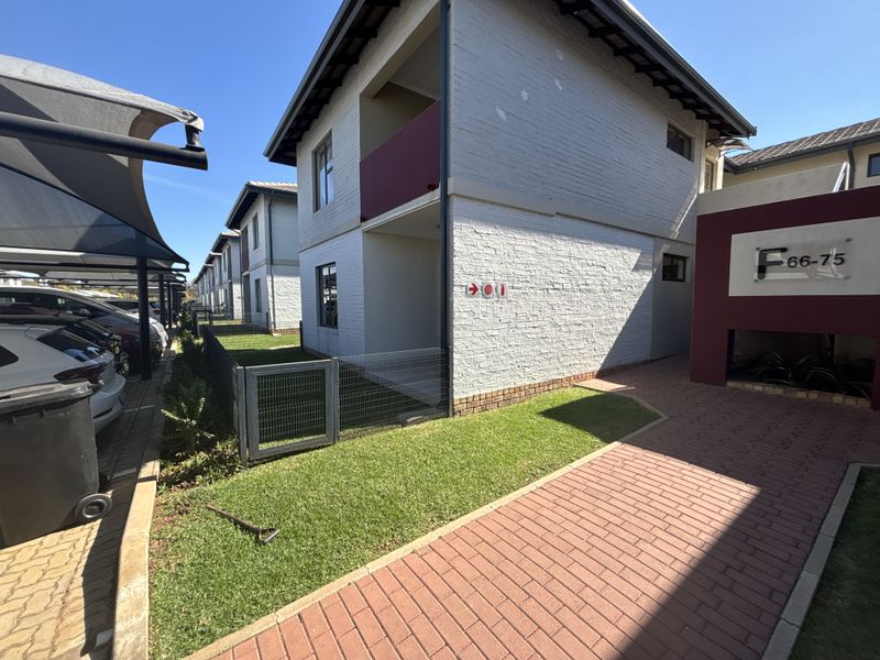 Exterior view of a townhouse complex featuring brick paving, a shade cloth carport, and a painted brick facade with a balcony.