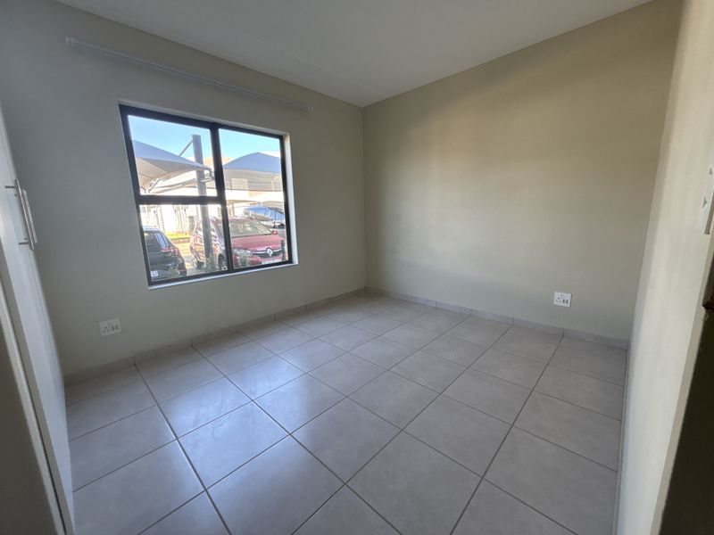 A clean, empty bedroom featuring neutral tiled flooring, built-in cupboard storage, and a large window providing natural light.