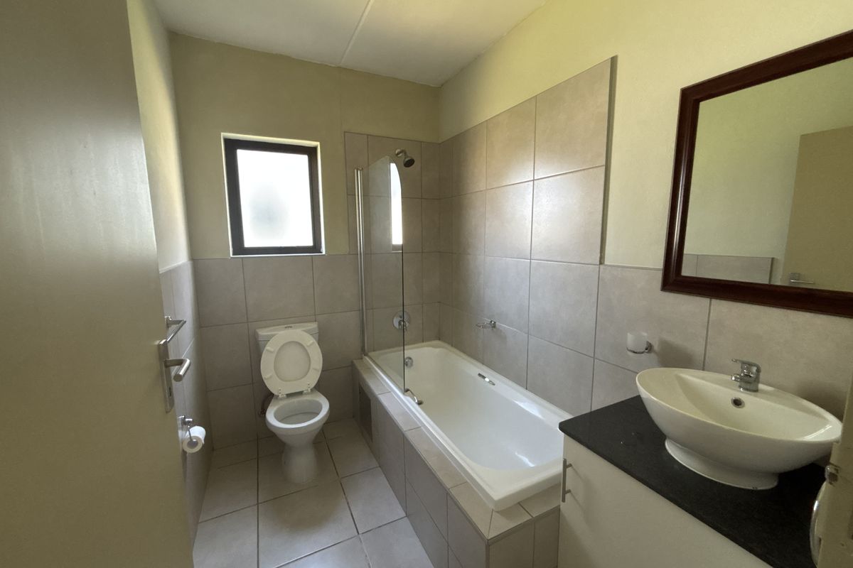 A functional bathroom featuring a built-in vanity with a vessel sink, a bathtub with a glass shower screen, and neutral wall and floor tiling.
