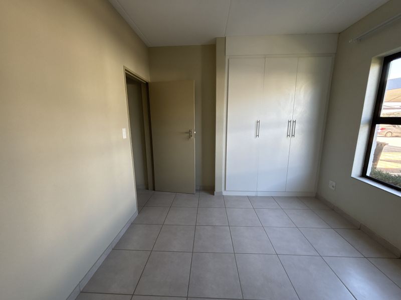 A clean, empty bedroom featuring neutral tiled flooring and white built-in cupboards, offering a blank canvas for personalization.