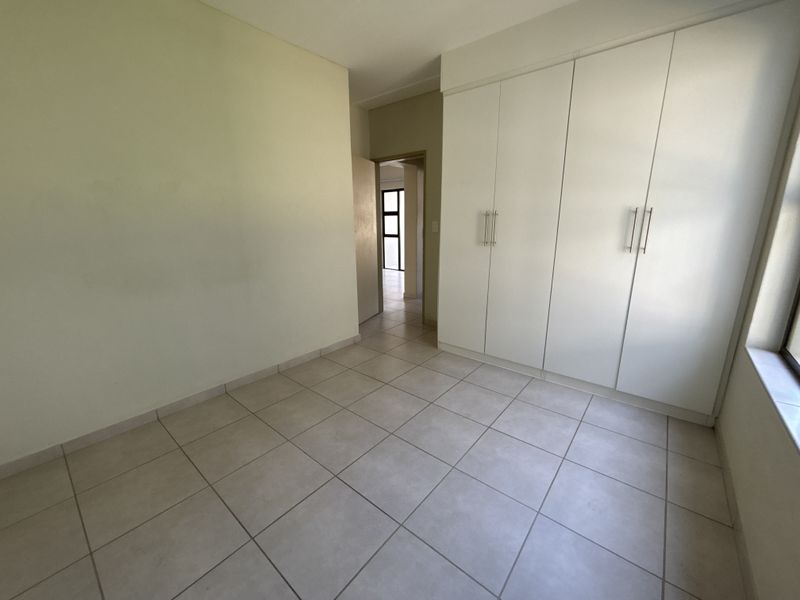An empty bedroom featuring neutral tiled flooring and built-in white cupboards, offering a clean and versatile space.
