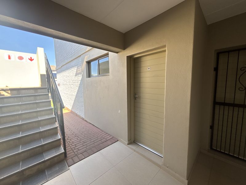 Entrance area of the townhouse featuring a tiled staircase with metal handrail, paved walkway, and a secure main entrance door.