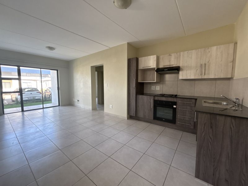 Open-plan living area featuring a modern kitchen with built-in cabinetry, oven, hob, and extractor fan, leading to a bright space with tiled flooring.