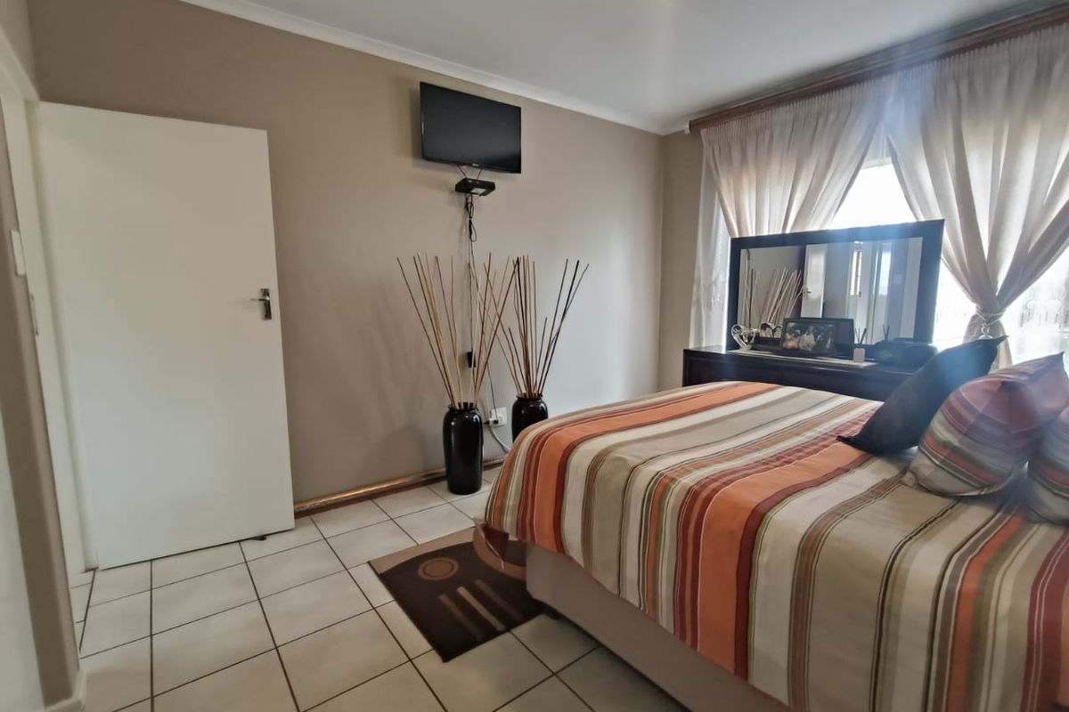 A bedroom featuring tiled flooring, neutral wall tones, and a window with curtain tracks, providing a functional and well-lit sleeping space.