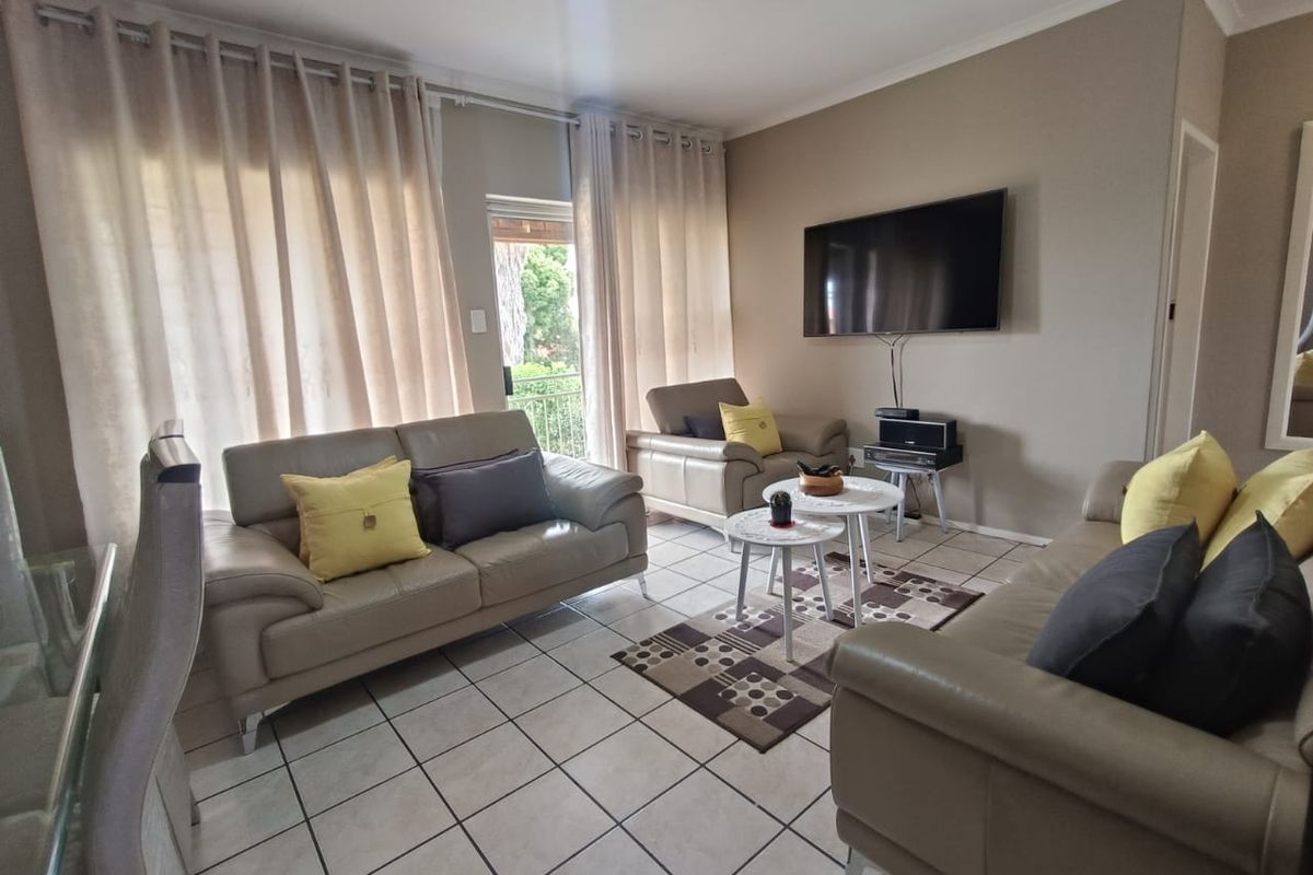 A comfortable living room featuring tiled flooring, neutral wall tones, and large sliding glass doors that provide access to an outdoor balcony area.