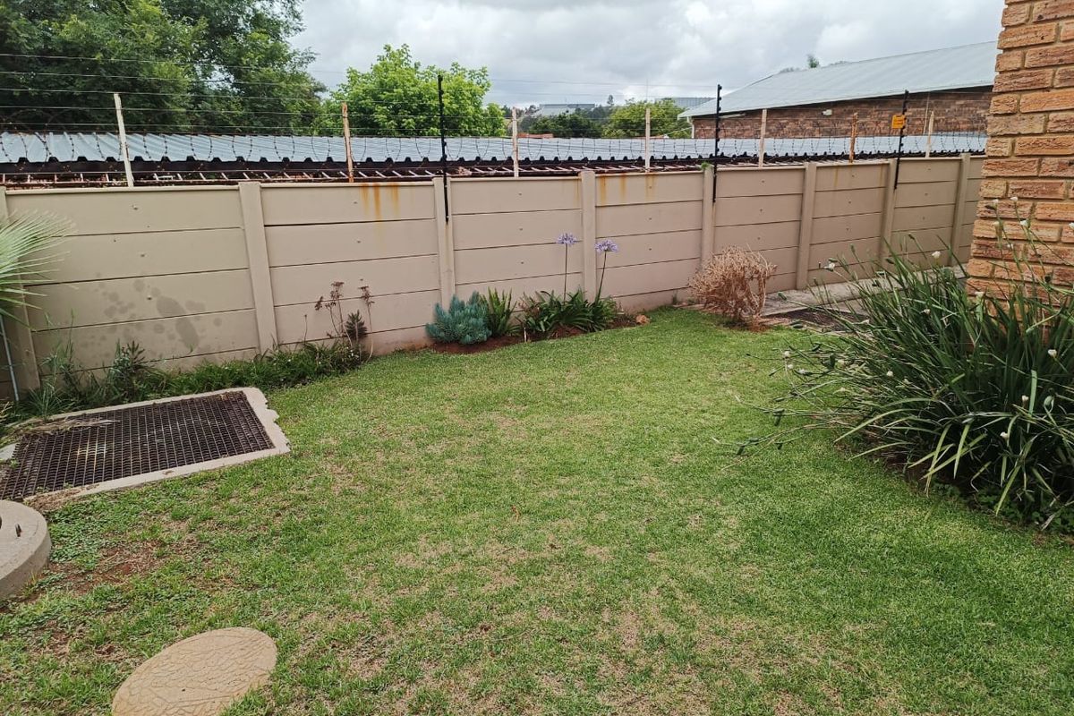 A private rear garden area featuring a lawn, established garden beds, and a perimeter boundary wall with electric fencing.