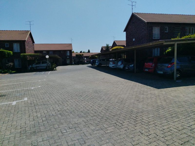 Exterior view of an apartment complex featuring a paved parking area and covered carports for residents.