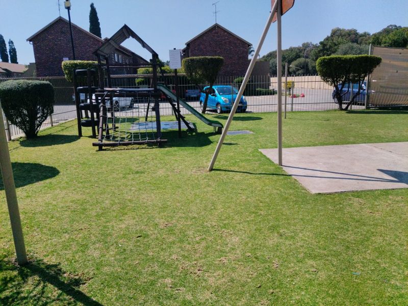 Communal garden area featuring a playground set, well-maintained lawn, and secure perimeter fencing within the apartment complex grounds.