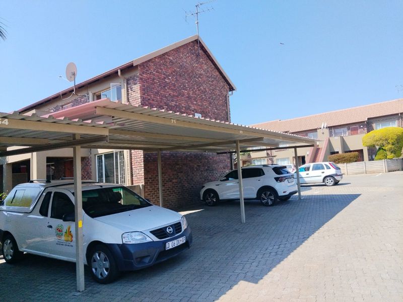 Exterior view of an apartment complex featuring a covered carport area with paved driveway and exposed brick building facade.
