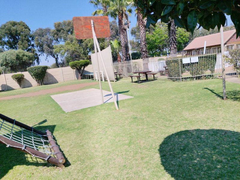 Outdoor communal sports area featuring a basketball hoop, concrete court section, and climbing equipment within a fenced garden setting.