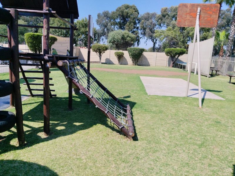 Communal outdoor recreational area featuring a playground structure, basketball hoop, and landscaped lawn within a fenced complex.