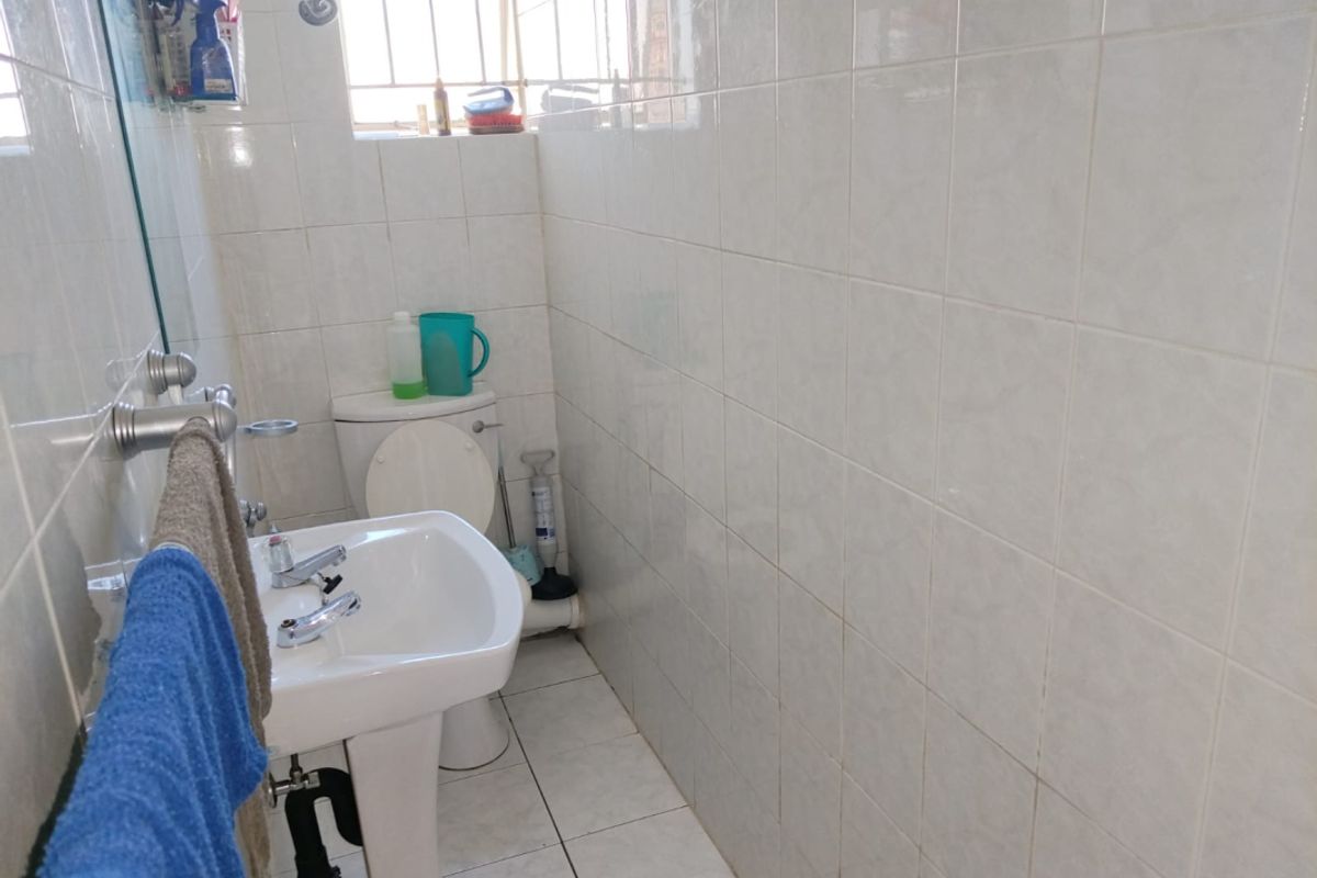 A functional bathroom featuring a pedestal basin, toilet, and full-height ceramic wall tiling with a window for natural light.