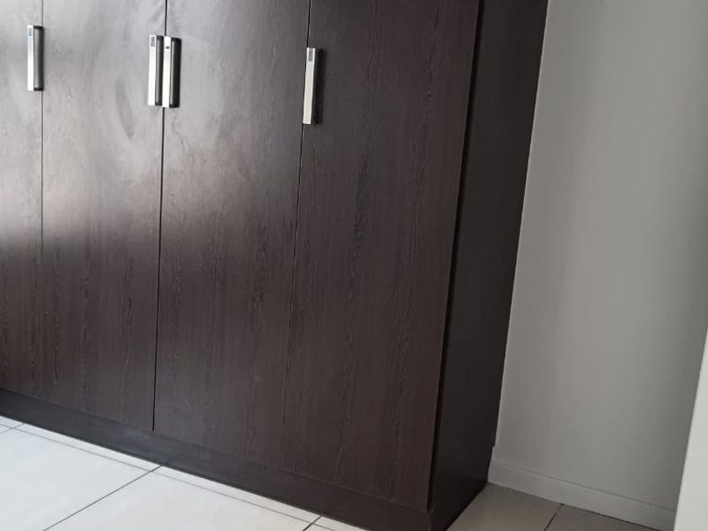 A clean bedroom featuring dark wood built-in cupboards, neutral tiled flooring, and a white panel door.