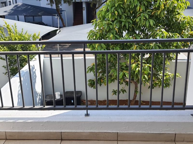 A private balcony featuring a metal balustrade and tiled flooring, overlooking the complex grounds and parking area.