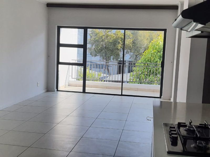 Spacious open-plan living area featuring tiled floors, a modern kitchen with gas hob, and large sliding doors leading to a private balcony.