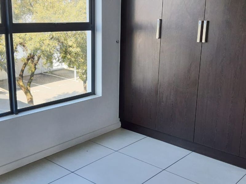 A bright, empty bedroom featuring tiled flooring and dark wood built-in cupboards, offering a clean and neutral space ready for personalization.