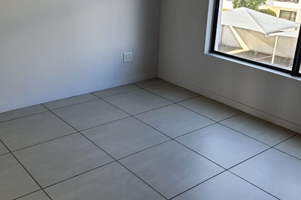 A bright, empty bedroom featuring neutral tiled flooring and a large window, providing a clean and versatile space ready for furnishing.