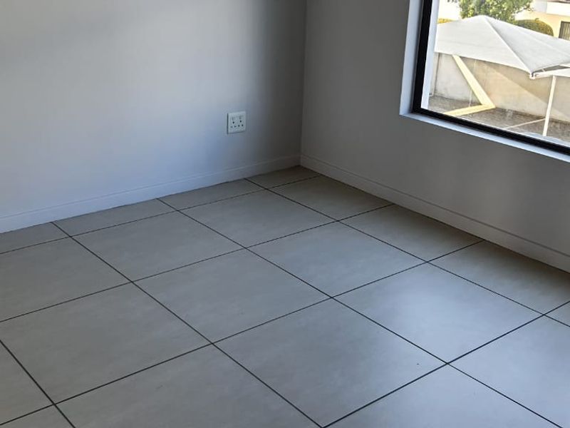 A bright, empty bedroom featuring neutral tiled flooring and a large window, providing a clean and versatile space ready for furnishing.