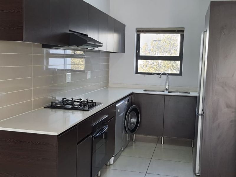 Modern kitchen featuring dark wood cabinetry, stone countertops, gas hob, built-in oven, extractor fan, and tiled splashback with integrated sink.