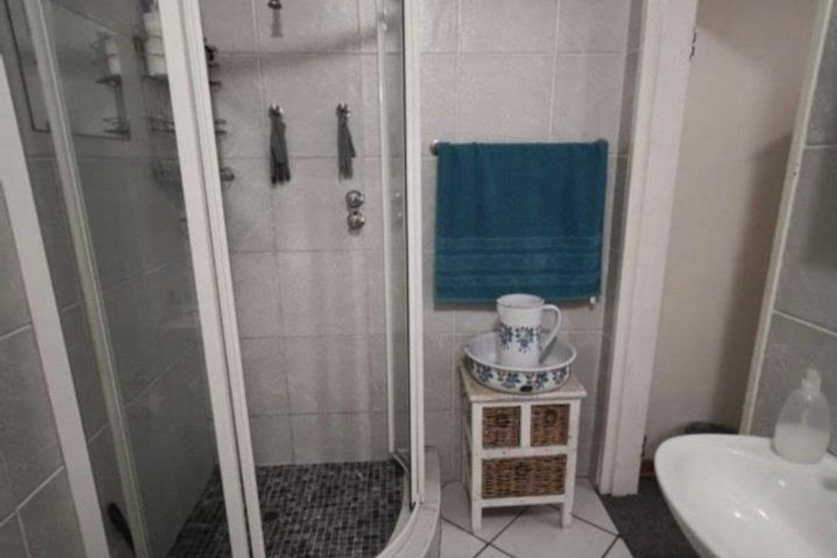 A functional bathroom featuring a curved shower enclosure, pedestal sink, and tiled finishes throughout.