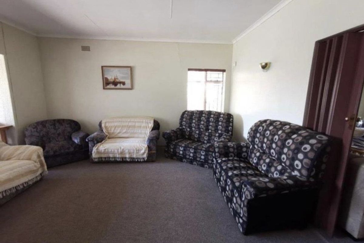 A living room featuring carpet flooring and wall-mounted lighting, showing signs of wear including visible cracks on the wall.