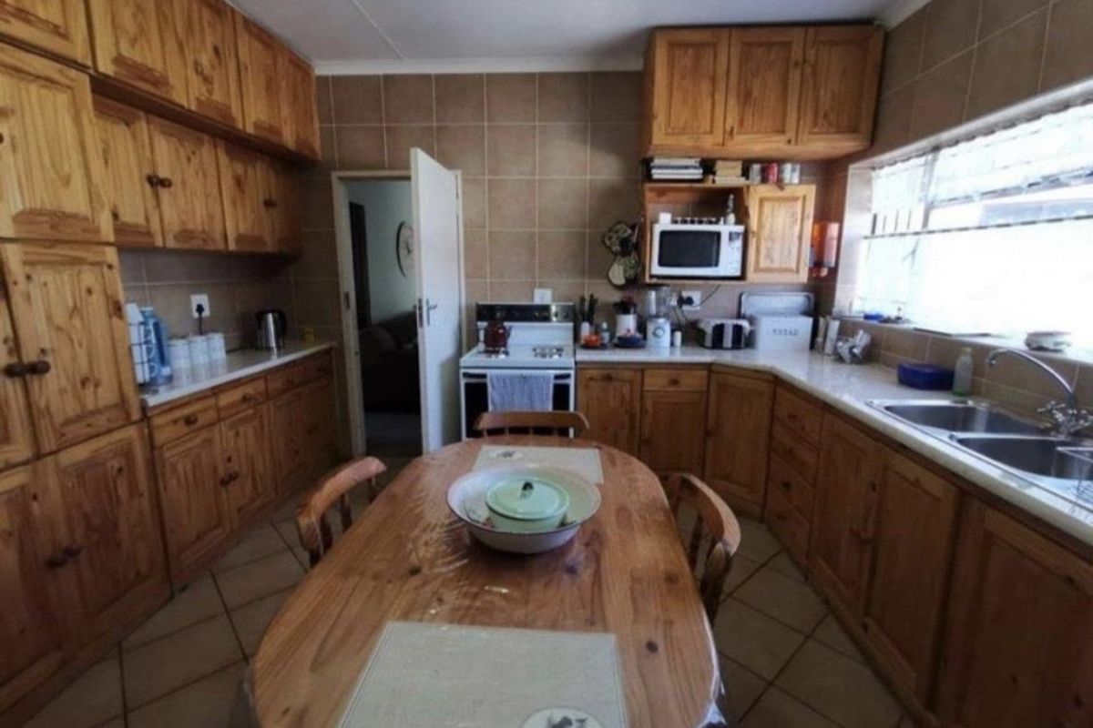 A functional kitchen featuring extensive wooden cabinetry, tiled backsplash, a double basin sink, and a freestanding stove with tiled flooring throughout.
