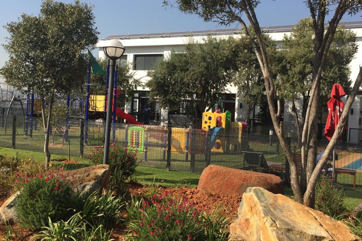 A well-maintained communal garden area featuring landscaped rock beds, mature trees, and a fenced playground facility for residents.