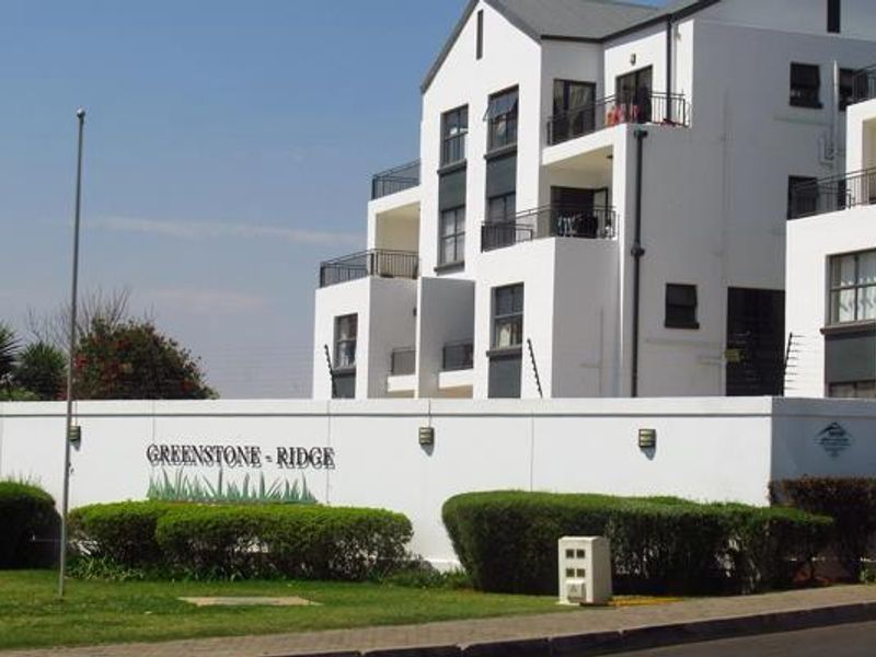 Front view of the Greenstone Ridge apartment complex, featuring modern white facades, balconies, and a secure perimeter wall with electric fencing.