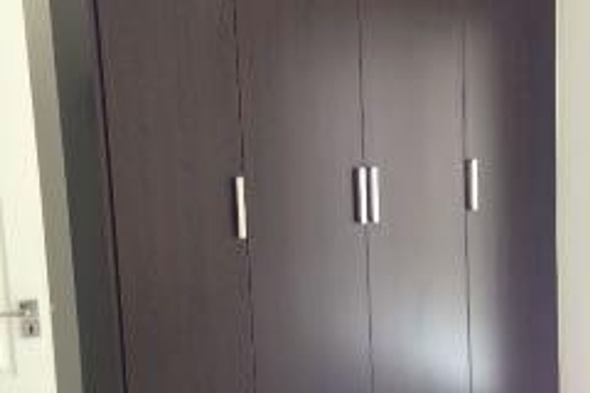 A bedroom featuring a large, dark wood-finish built-in wardrobe with modern metal handles and tiled flooring.
