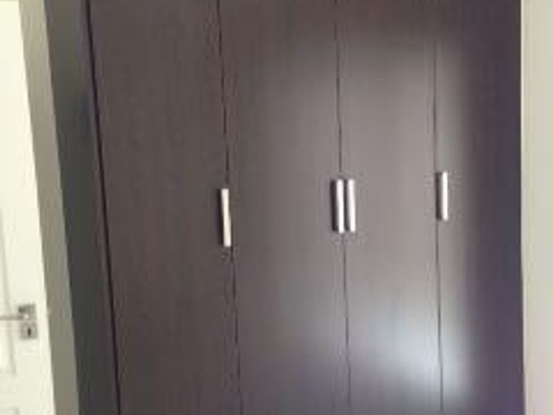 A bedroom featuring a large, dark wood-finish built-in wardrobe with modern metal handles and tiled flooring.
