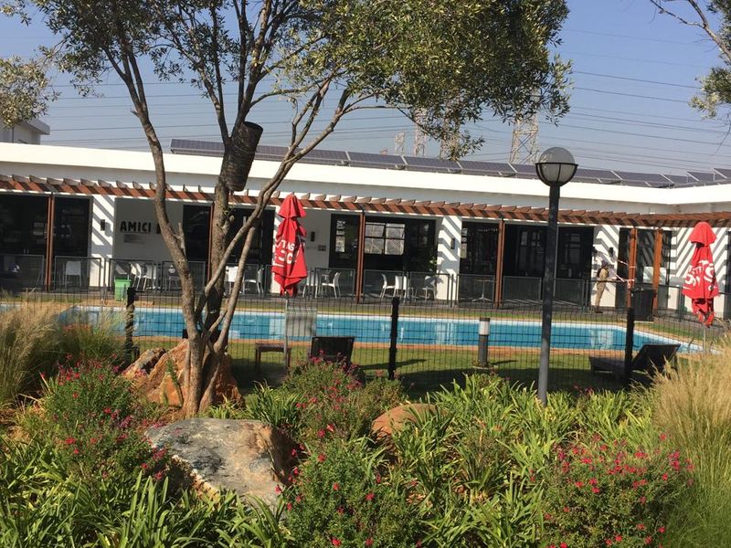 A well-maintained outdoor pool area featuring a swimming pool, pergola structure, solar panels, and landscaped garden surroundings.