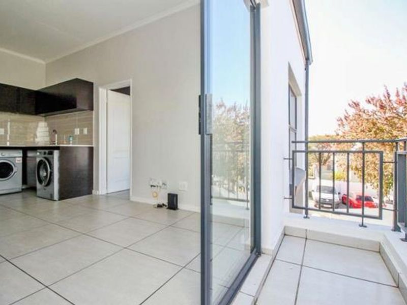 Open-plan kitchen area featuring tiled floors, built-in cabinetry with integrated laundry appliances, and direct access to a private balcony through sliding glass doors.