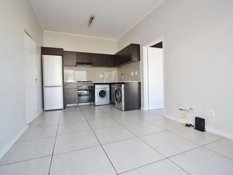 An open-plan living and kitchen area featuring neutral tiled flooring, dark cabinetry, and integrated kitchen appliances in a clean, vacant space.