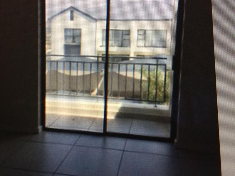 An empty living area featuring tiled flooring and a sliding glass door that opens onto a balcony with a metal balustrade.