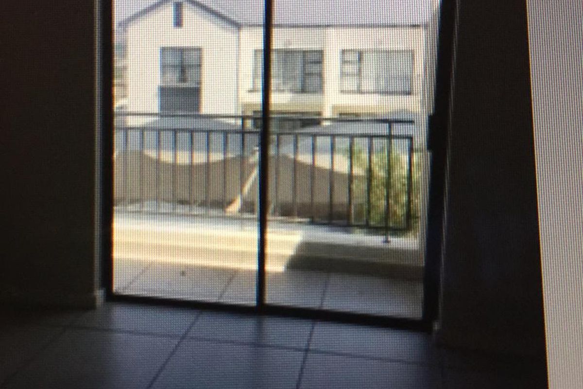 An empty living area featuring tiled flooring and a sliding glass door that opens onto a balcony with a metal balustrade.