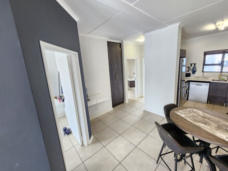 An open-plan living and kitchen area featuring neutral tiled flooring, modern cabinetry, and a functional layout connecting to adjacent rooms.