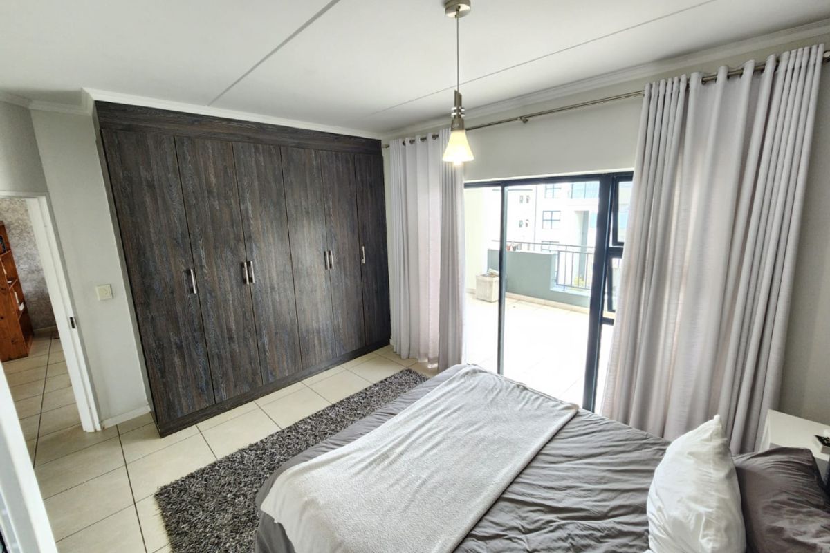 A well-maintained bedroom featuring dark wood built-in cupboards, tiled flooring, and a sliding glass door providing access to a private balcony.