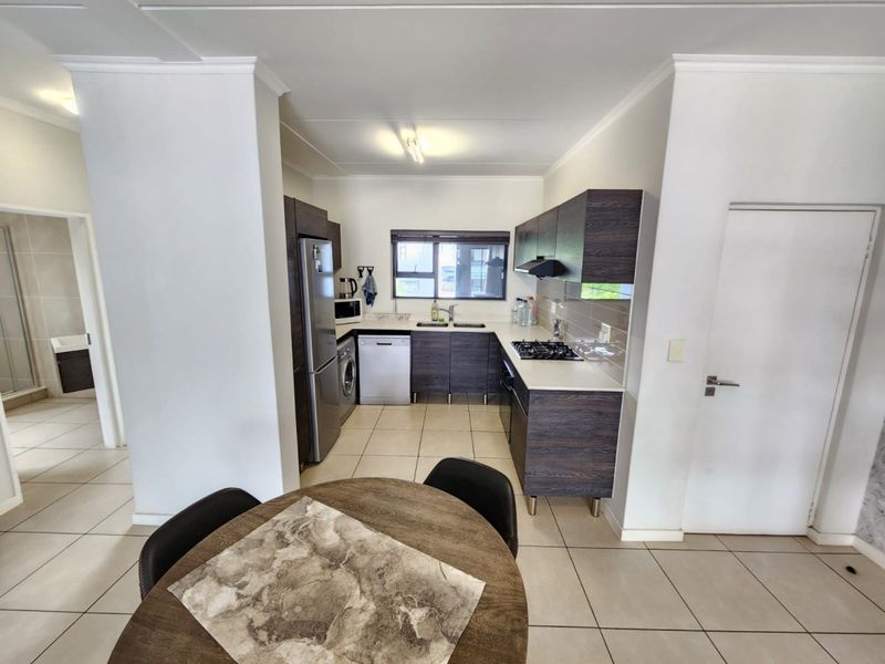 A functional kitchen featuring dark wood-finish cabinetry, a gas hob, extractor fan, and tiled flooring, seamlessly integrated into the open-plan living area.